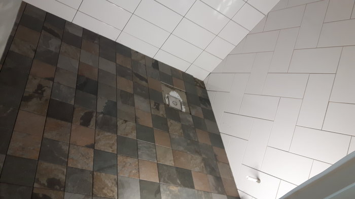 Delvis lagt klinkergolv möter en vit kaklad vägg i fiskbensmönster, några plattor och fog saknas.