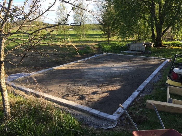 Nyinstallerad kantsten runt en grusgång eller planteringsyta i en trädgård med träd och landskap i bakgrunden.