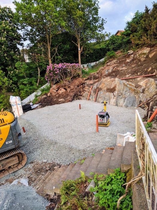 Nyutlagd makadam med rör och paddningsmaskin på en sluttning i ett trädgårdsbyggprojekt.