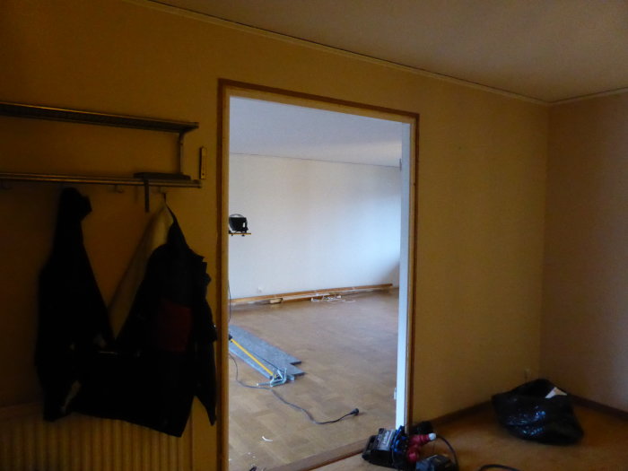 Utsikt från hall med befintliga kläder och verktyg mot ett tomt rum före renovering.