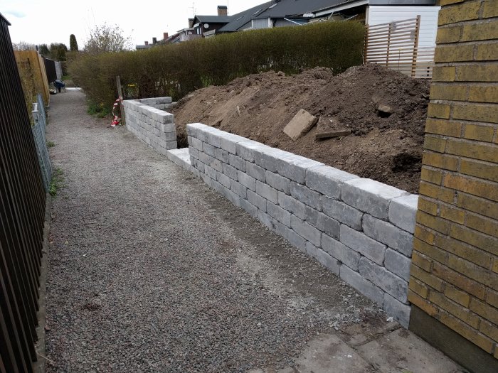 Nybyggd stödmur av gråa betongblock längs med grusgång och jordhög bakom.