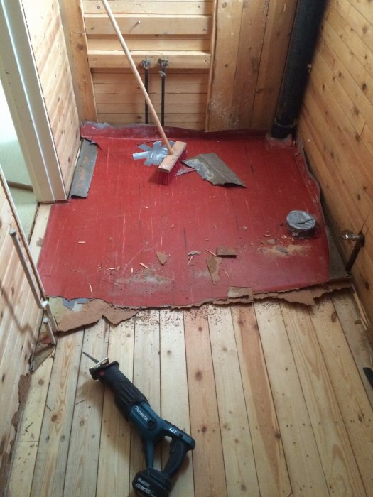 Rivningsarbete i badrum med röda skivor på golvet, spillror, och en eldriven såg.