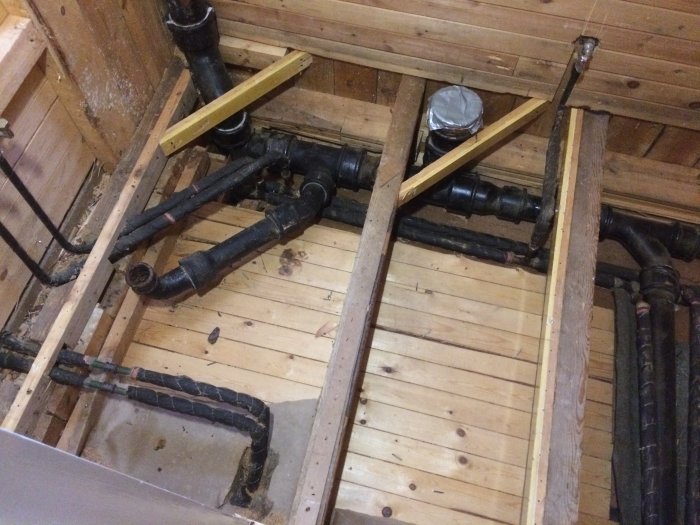 Rivet badrumsgolv med exponerade avloppsrör och träbjälkar under renoveringsprocessen.