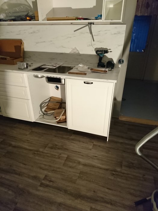 Kök under renovering med öppna lådor, nya vitvaror och verktyg på arbetsbänken.