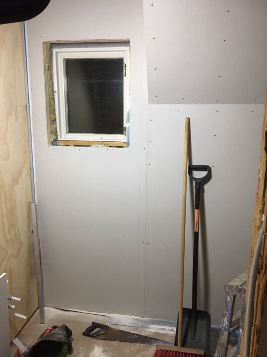 Riktade och spikraka gipsskivor på vägg med fönster och verktyg på golvet i ett pågående byggprojekt.