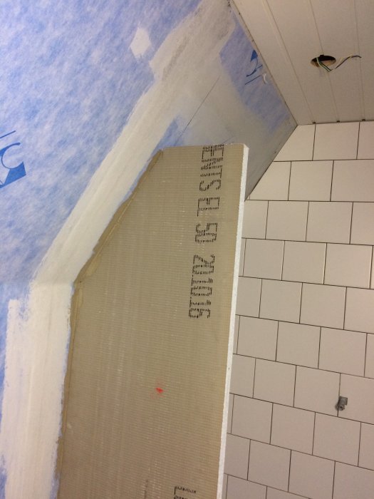 Hörn av badrum under renovering med applicerat tätskikt och nyinstallerat vitt kakel.
