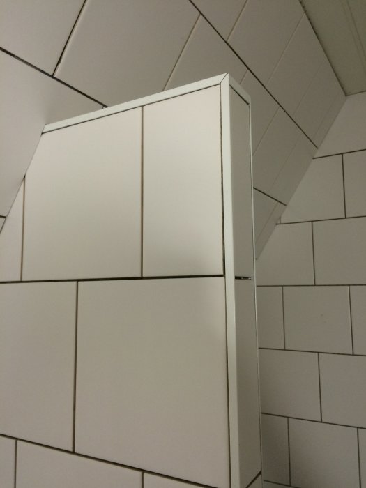 Nyinstallerad vit kakelvägg med spikrak fogning och sitthylla med aluminiumlist i ett badrum under renovering.