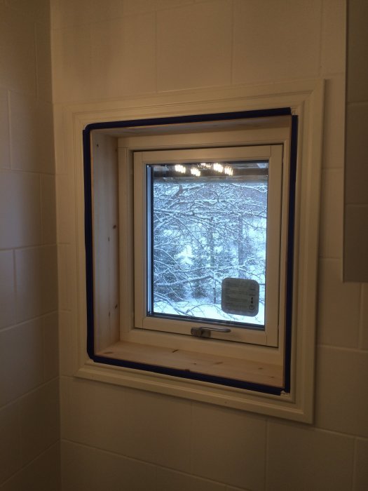 Nytt utbytt fönster i badrum med vita kaklade väggar och utsikt till snötäckta träd.