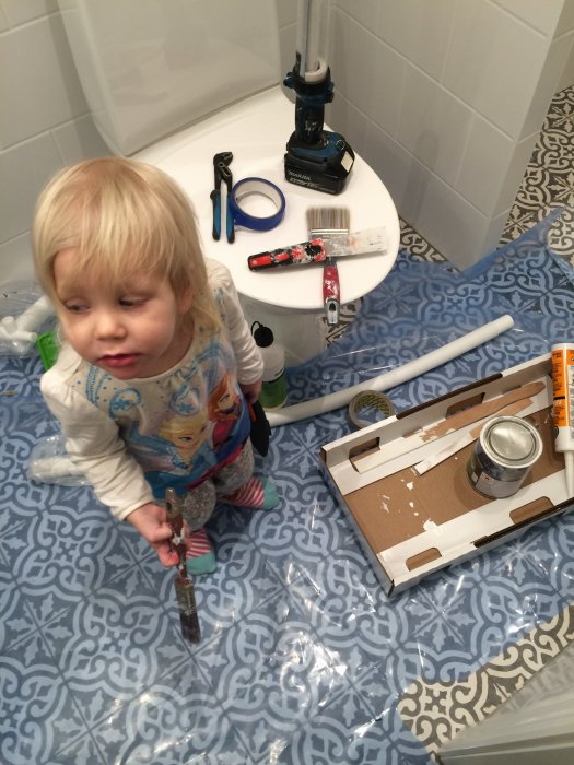 Barn står på nytt badrumsgolv bland verktyg och installationsmaterial.
