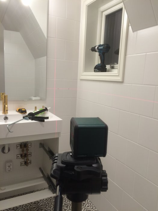 Nyrenoverat badrum med laserkors för installation, borrskruvdragare på fönsterbräda och verktyg på handfat.