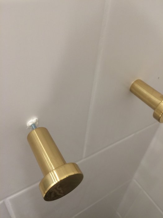 Två guldiga krokar monterade på en vit kakelvägg, en del i ett diy-projekt i ett badrum.