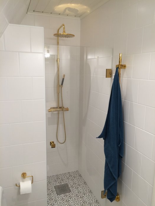 Modern duschhörna med vita kakelväggar, mässingsdetaljer och mönstrat golv.