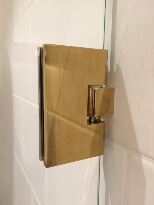 Mässingsdetalj för dusch från Tapwell monterad på vit kaklad vägg, visar vattenreglage och patina.