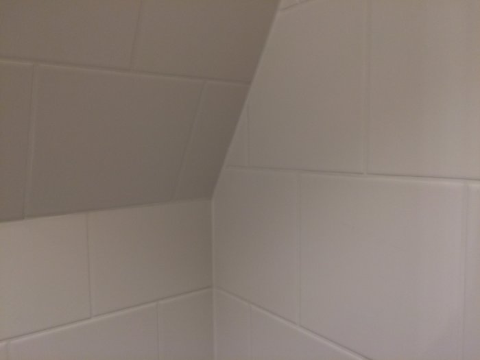 Väggdetalj med kakel och dolda installationer bakom badrumsinredning.