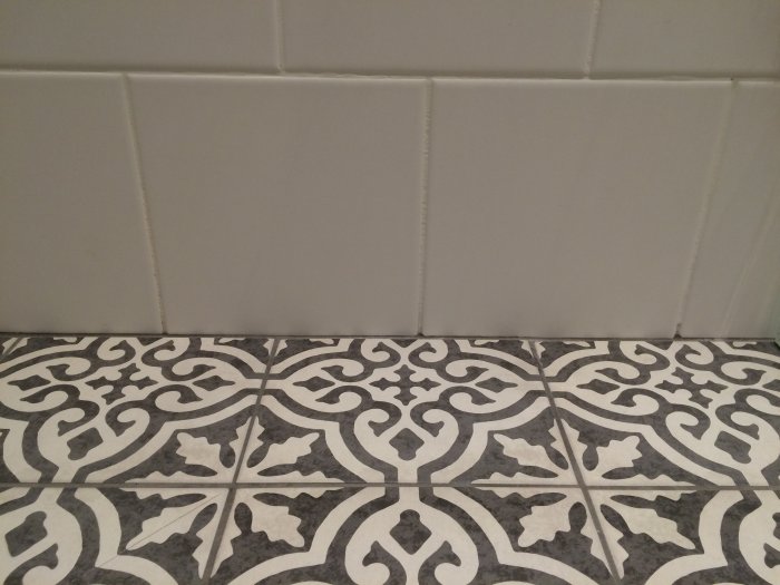 Vägg möter mönstrat golv; vita kakelplattor ovanför svartvita, dekorativa klinkerplattor.