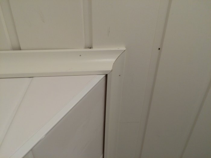 Vit list som löper längs en kommod och vägg, med en slät och ren finish i en hörna av rummet.