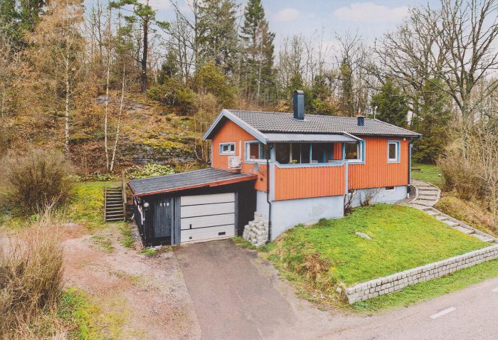 Ett orange enfamiljshus med svart tak och garage, omgivet av grönska och en uppfart.