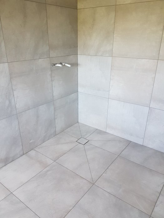 Renoverad duschhörna med kaklade väggar och golv, samt en installerad duschblandare.