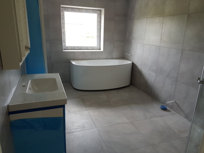 Renoverat badrum med grå kakel, fristående badkar och handfat under montering.