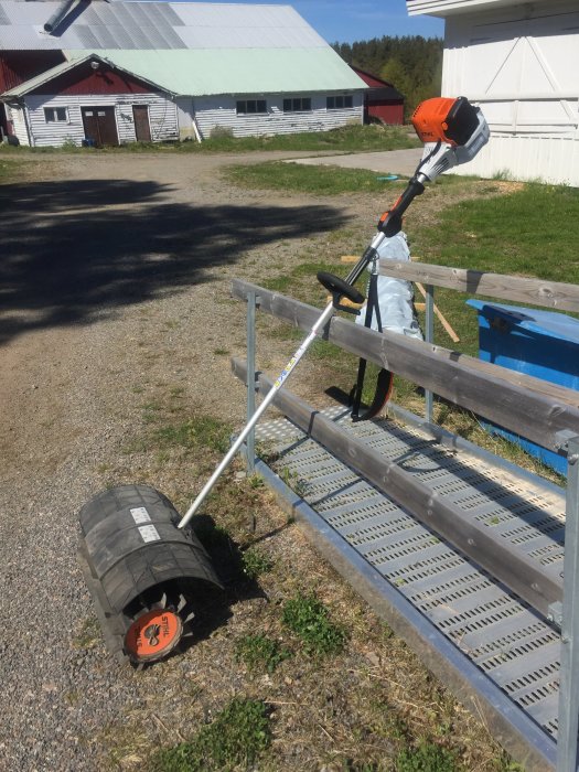 Motoriserad sop och trimmerhuvud liggande på en metallpall framför en lada.