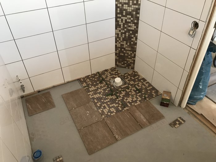 Pågående badrumsrenovering med utlagda men ej fastsatta klinkers och mosaik.