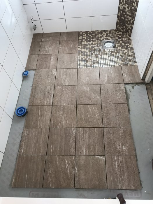 Delvis lagda klinkerplattor och mosaik i en duschhörna under renovering.