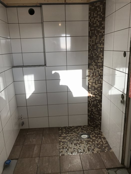 Klinker- och mosaikläggning i en duschhörna under renovering.