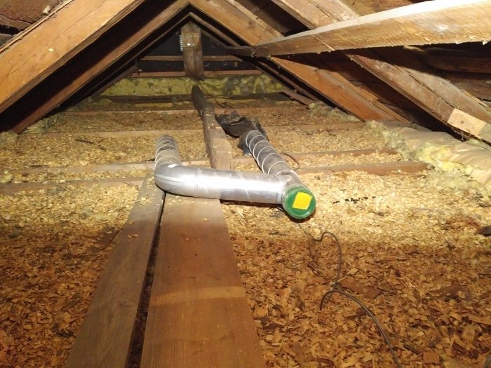 Vindutrymme med isolering, synliga takbjälkar och ventilationsrör över bjälklaget.
