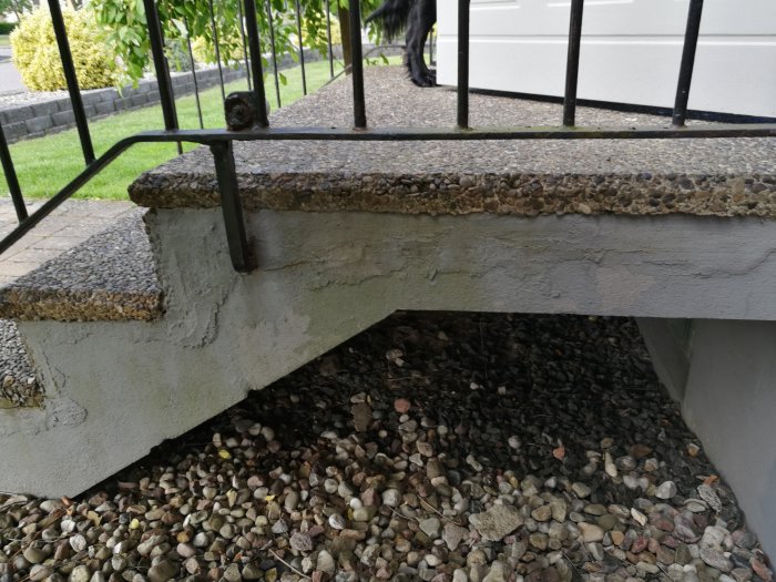 Bild på en skadad entrétrappa med sprucken och släppt lagning på betongytan och grusunderlag.