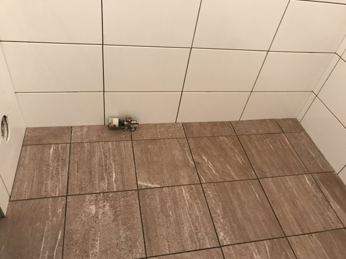 Nylagd klinkergolv i brunt mönster intill vita kakelväggar med väntande mosaikinstallation.