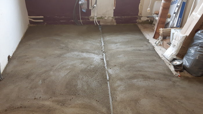Nyjuten cementgolv i rum med en synlig skarvlinje och byggmaterial längs väggarna.