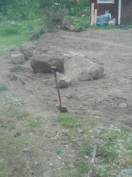 En grävd plats med stora stenbumlingar och en spade indikerar förberedelse för utbyggnad av en 3x4m yta.