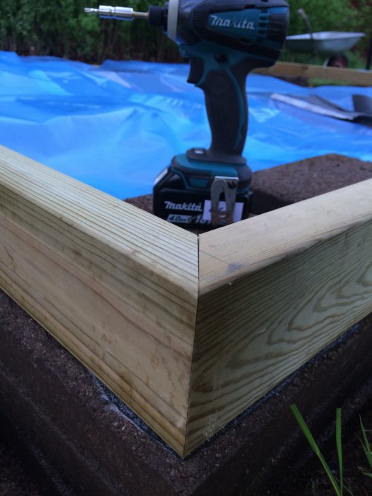 Trähörn av bjälklag på tralldäck med Makita-skruvdragare ovanpå, blå plast i bakgrunden.