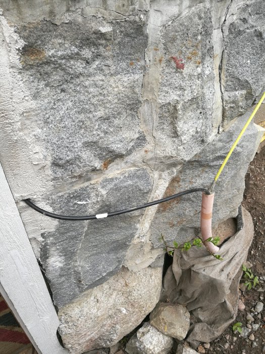 Sloppigt installerad gul fiberkabel och svart kabel längs en stenvägg och in genom rör.