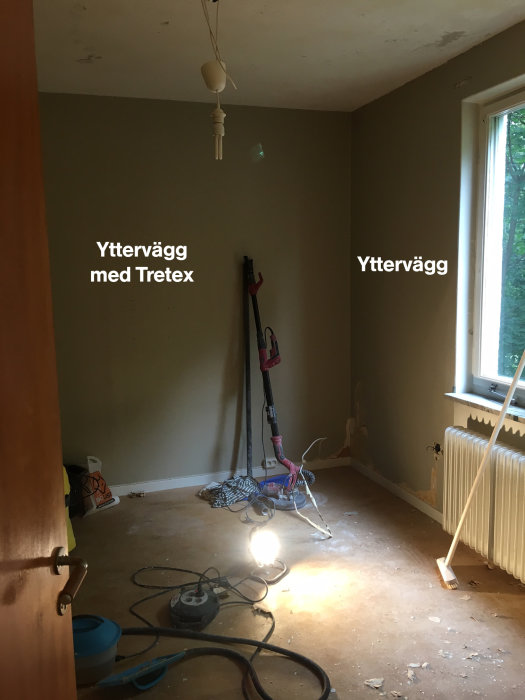 Renoveringsprojekt i sovrum med tretex på en yttervägg, avrivna tapeter och byggmaterial på golvet.