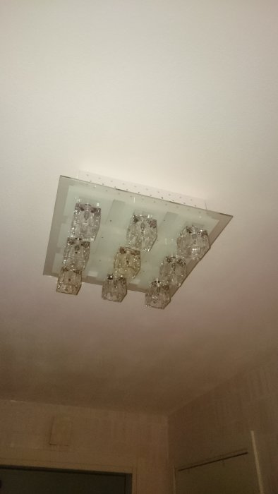 Taklampa med kristalliknande utseende tänd, monterad på ett vitt tak.
