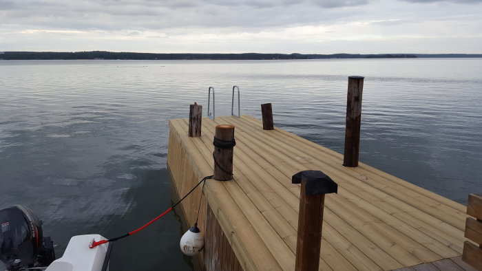 Nybyggd träbrygga som sträcker sig ut i lugnt vatten med skog i bakgrunden.