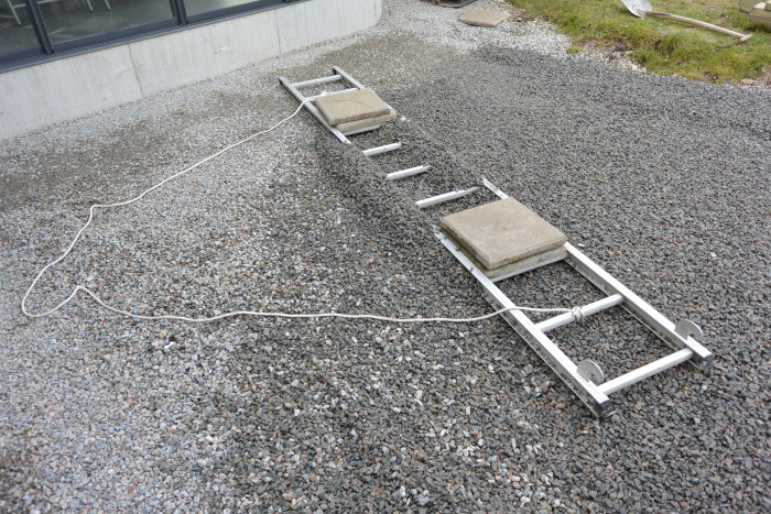 Gamla cementplattor utlagda på en gångväg av singel med hjälp av ett verktyg och distansklossar för justering.