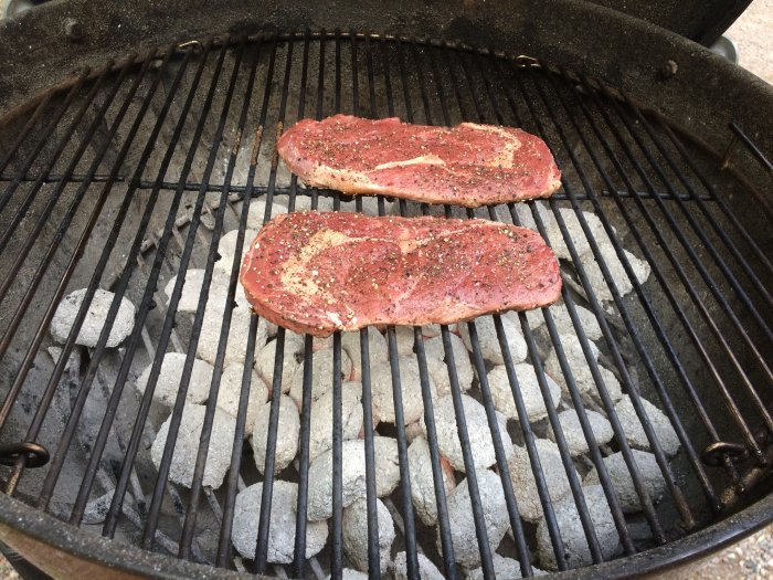 Två kryddade biffar på grillgallret ovanför glödande kol.