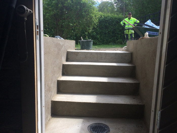 Nybyggda betongtrappor sett från en dörröppning, arbetare med skottkärra i bakgrunden.