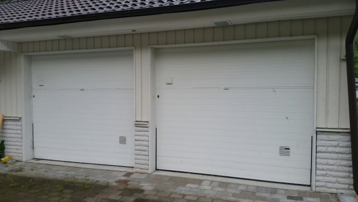 Två vita garageportar på ett hus med vitputsade väggar och svart tak.