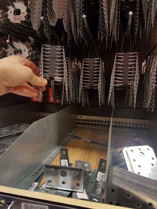 En hand pekar mot olika typer av balkskor som hänger på en försäljningsställning i en byggmarknad.