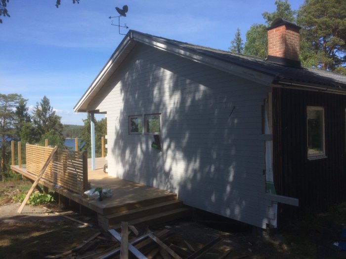 Nypanelad gavelspets på hus med utsikt över en sjö och en nybyggd trädäck.