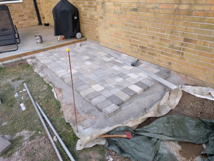 Nästan färdigställd grillplats med gatstenar, verktyg och byggmaterial synliga.