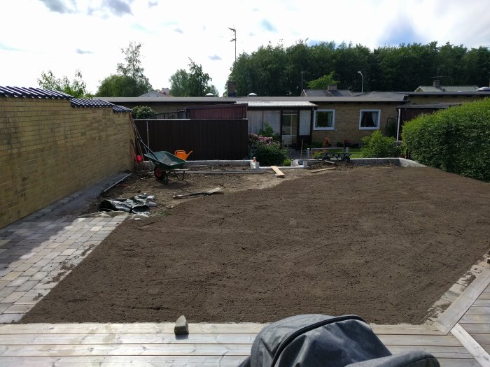 Trädgård under konstruktion med nylagt stenparti, jordhög, skottkärra och framtida planteringytor.