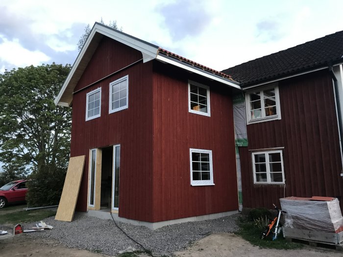 Röd trävilla under renovering med omonterade fönsterramar och byggmaterial framför huset.