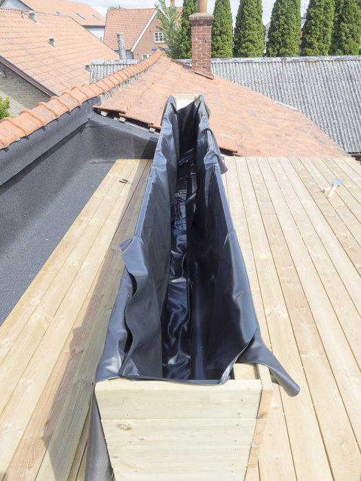 Installation av svart dammfolie på en träkonstruktion av ett byggprojekt med hus och himmel i bakgrunden.