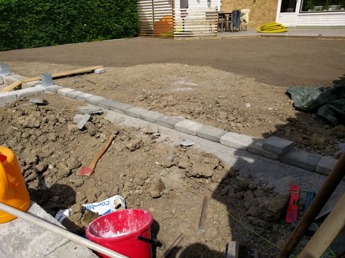 Nyjordad gräsplan och stensatt kant vid trädgårdsrenovering, med verktyg synliga.
