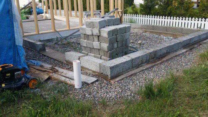 Betongklack som är 4 cm för låg, med staplade stenblock och byggmaterial i en trädgård.