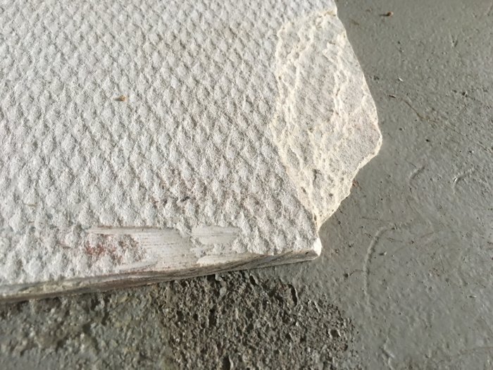 Skadad kant på ett vitt isolerande byggmaterial mot en betongyta.